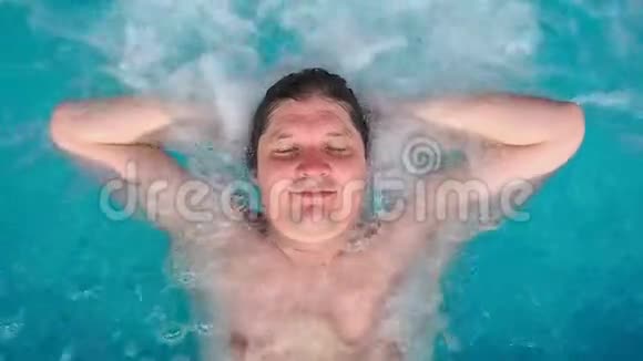 这个人躺在按摩浴缸里放松看着相机白种人躺在游泳池里躺在水里视图视频的预览图