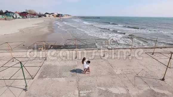 在海的背景下那个男人在海滩上旋转女孩的正面景色视频的预览图