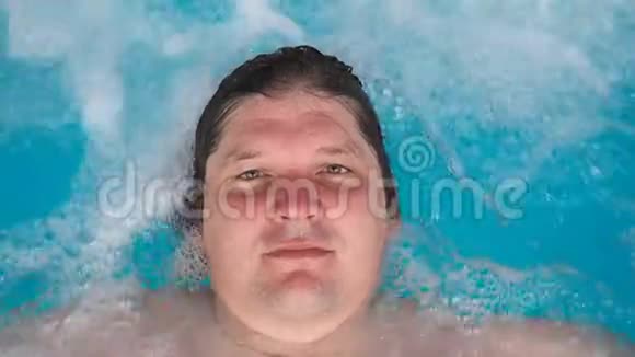 男人躺在按摩浴缸里放松看着相机白种人在水上的泳池里休息视图视频的预览图