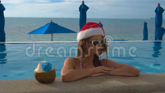 年轻的白种人穿着圣诞帽在游泳池里放松热带国家的圣诞节视频的预览图