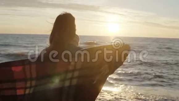 年轻女子带着格子花格子伸展双臂在多风的海滩上享受日落自由概念视频的预览图