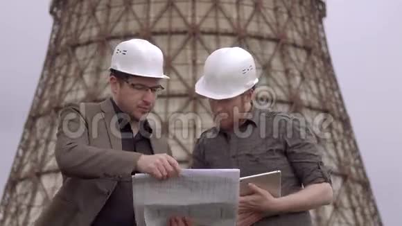 两个商人在核电站的背景上戴着头盔一座建筑的建筑师视频的预览图