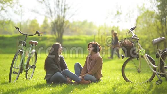 深色头发的女孩喜欢坐在自行车附近的绿草和公园里的树木上野餐女青年视频的预览图