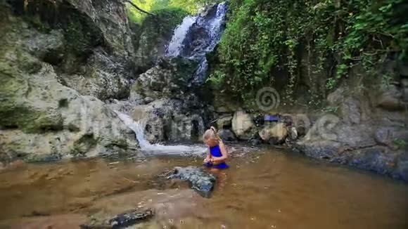 小金发女郎在瀑布附近的水中嬉戏视频的预览图