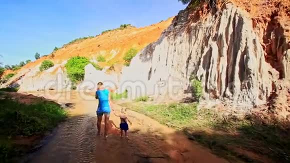 母亲小女孩在水中漫步走过陡峭的橙色悬崖视频的预览图