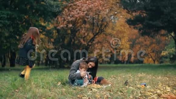 秋天公园的家人有趣可爱的小女孩把秋天的黄叶扔给她的妈妈和弟弟小男孩慢了视频的预览图