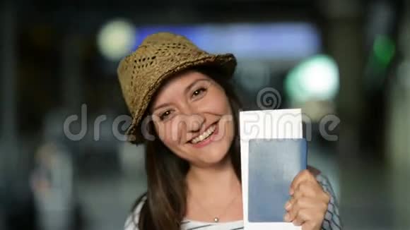 夏帽中迷人的微笑布鲁内特在机场等待她的飞机的特写镜头并附有机票和视频的预览图