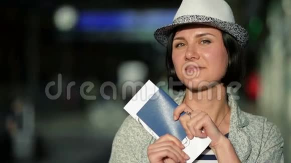 戴着短黑头发和夏帽的年轻女子拿着护照和机票看着镜头微笑着视频的预览图