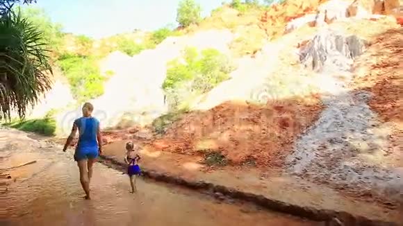 小金发姑娘在母亲身边的溪水旁奔跑视频的预览图