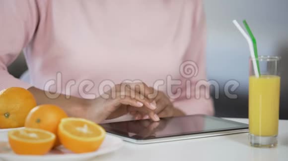 女孩在平板电脑上打字橘子和新鲜果汁在桌子上博客关于节食视频的预览图