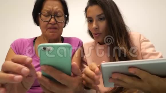 高级混合种族妇女学习如何使用手机退休的母亲和年轻的女儿使用现代小玩意4K视频的预览图