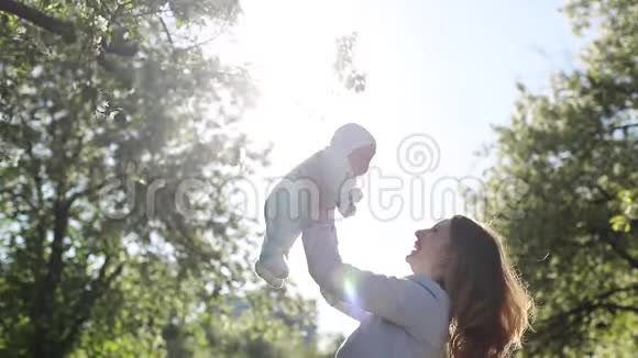 妈妈把她可爱的宝宝举得高高的在公园里玩耍和微笑视频的预览图