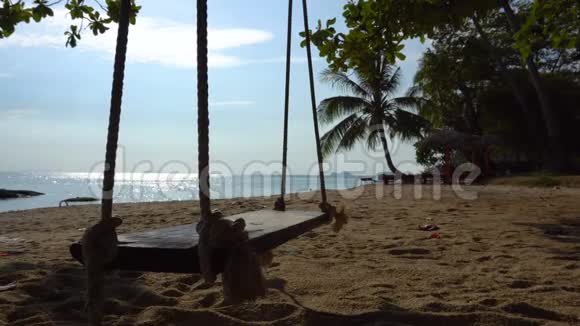 在温暖的热带海洋成本的沙滩上一个棕榈树上的绳索秋千悬挂视频的预览图
