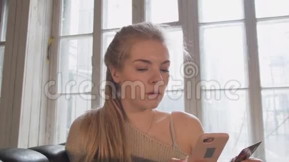 一个漂亮的金发女郎正通过坐在窗户前的椅子上的电话购买信用卡A视频的预览图