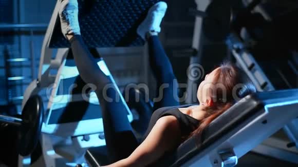 那个女孩正在健身房训练腿按在模拟器中用于大腿和臀部的背部视频的预览图