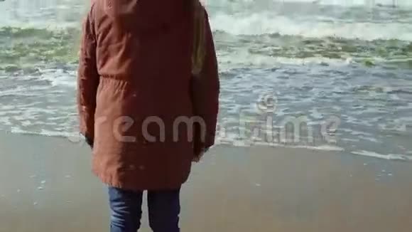 穿着黄色胶靴的可爱小女孩站在海边望着远处跳了起来后视图视频的预览图