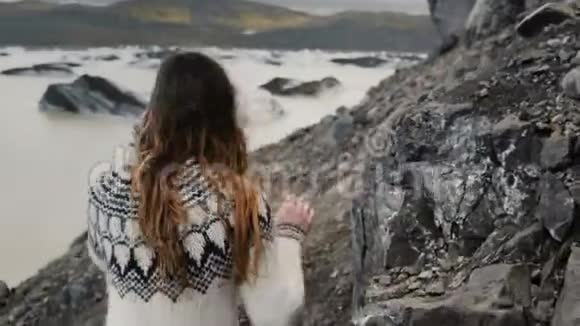 在冰岛瓦特纳霍卡尔冰川泻湖附近的岩石上徒步旅行的年轻旅游妇女的后景视频的预览图