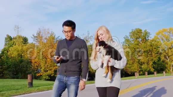 年轻的多民族夫妇在公园里散步一位亚裔男子在电话中交谈她靠近一名白人女子与一名男子同行视频的预览图