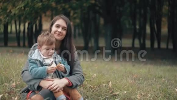 年轻漂亮的妈妈和她可爱的小儿子玩她正坐在秋天公园的膝盖上视频的预览图