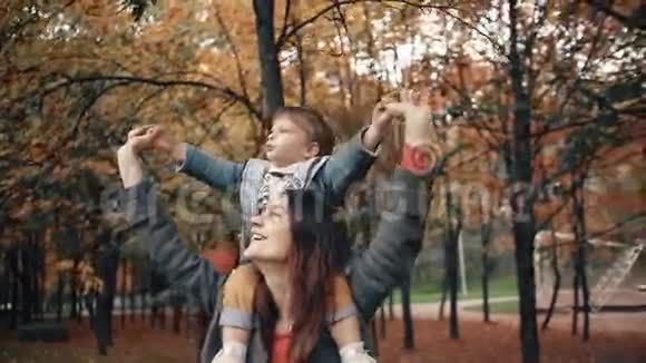 美丽的年轻妈妈抱着一个可爱的小儿子男孩用手指指着秋天公园里的东西视频的预览图