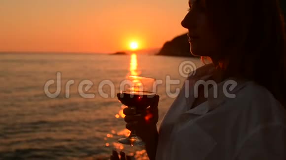 年轻女子从酒杯里喝红酒海边日落视频的预览图