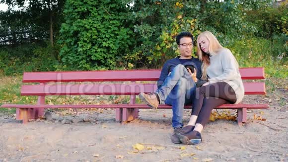 两个年轻的学生在公园的长凳上聊天好好享受平板电脑韩国男人和高加索女人视频的预览图