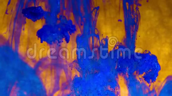 蓝色的墨水在金色的水中闪闪发光闪烁的油漆反应产生抽象的云层形成闪亮的背景视频的预览图