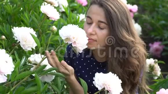美丽的女人闻着夏天花园里的一朵白牡丹花视频的预览图