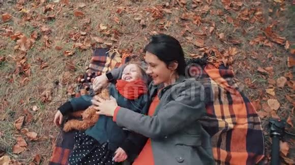 美丽的母亲和她可爱的小女儿躺在格子布上在秋天公园玩得很开心视频的预览图