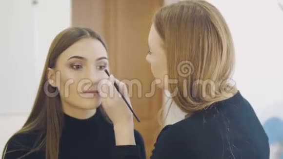 专业化妆师在白色房间内将眼线涂在模特的整个眼睛上美容化妆和时尚视频的预览图