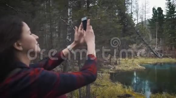 快乐女孩旅行者坐在岩石上在智能手机山坑湖上拍照穿着牛仔裤徒步旅行视频的预览图