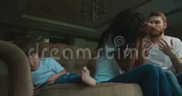 多种族家庭正在发生冲突而小儿子正在玩手机躺在沙发上情感视频的预览图