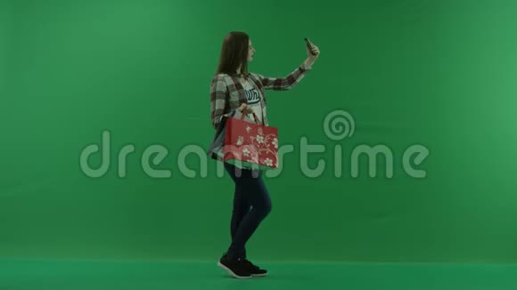 穿着购物袋的女孩站在她的右边在绿色屏幕上自拍视频的预览图