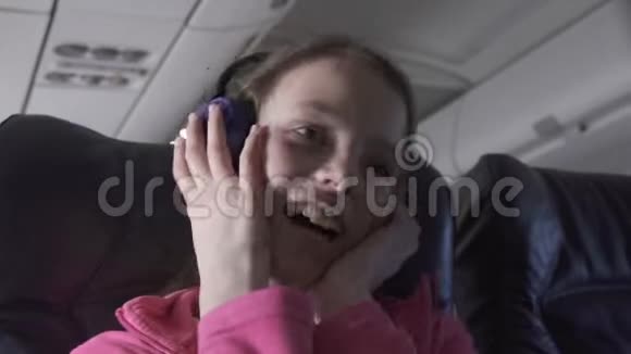 快乐的少女在飞机舱内听耳机上的音乐在旅行时听股票录像视频的预览图
