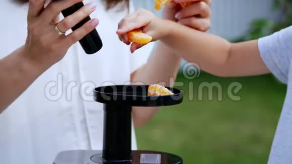 夏天在花园里母亲和四岁的儿子用曼达林做新鲜果汁把普通话片放进榨汁机里视频的预览图