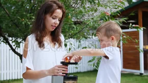夏天在花园里母亲和四岁的儿子用新鲜的山茱萸汁把柑桔片放进榨汁机里视频的预览图