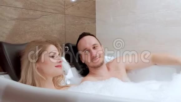 年轻夫妇男人和女人用泡沫躺在浴室里放松入住酒店视频的预览图