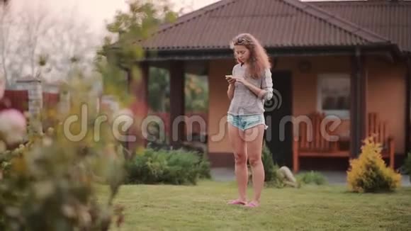 美丽的年轻女子站在后院使用智能手机女性在手机上浏览互联网视频的预览图