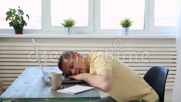 自由职业程序员在带笔记本电脑的办公桌上因疲劳而睡着视频的预览图
