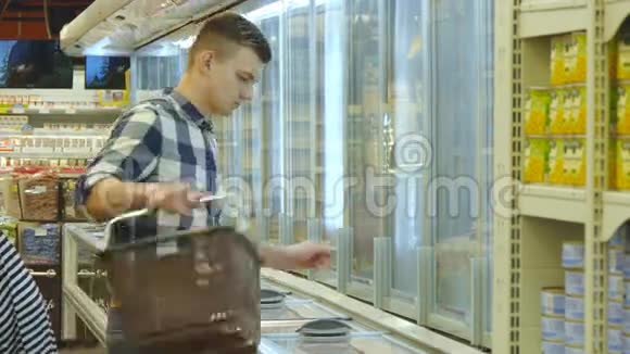 带着购物车的年轻人在冷藏区的超市买奶制品或冷藏食品视频的预览图