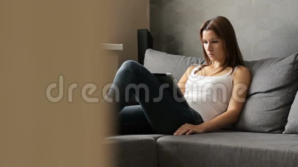 带电片的女人有平板电脑的女人坐在沙发上女士使用带有触摸屏的平板设备派克视频的预览图