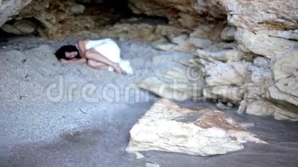 一个受惊的女孩躺在石洞里的沙子上视频的预览图