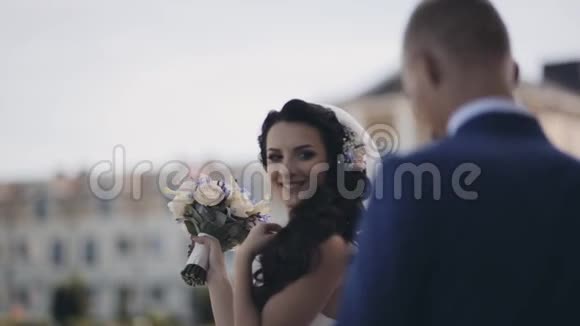 快乐的黑发新娘站在外面微笑金发新郎接近女孩和亲吻婚礼日视频的预览图