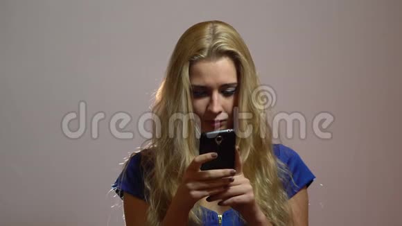 美丽的金发女孩穿着蓝色服装聊天与电话工作室视频的预览图