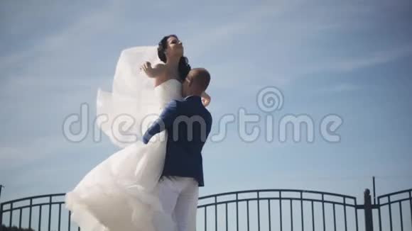 快乐的新郎牵着他的新娘穿着白色婚纱转过身来新婚夫妇享受晴天慢动作视频的预览图
