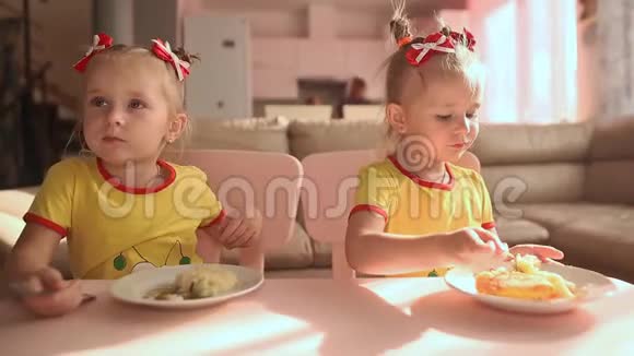 两个穿着黄色T恤的小可爱双胞胎姐妹正一起在房子厨房的桌子上吃食物视频的预览图