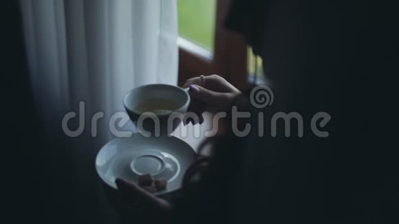 近景的黑发女人望着远处喝着茶女人一个人在家里度过早晨视频的预览图