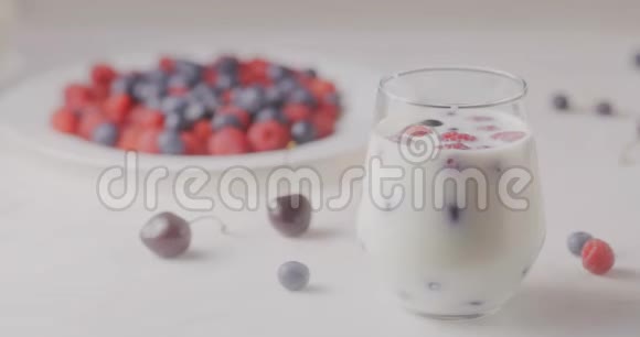 从一个有浆果和牛奶的玻璃杯中调焦放在一个有成熟蓝莓和樱桃的盘子里视频的预览图