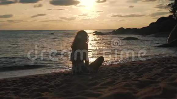 日落时坐在沙滩上度假的女孩视频的预览图
