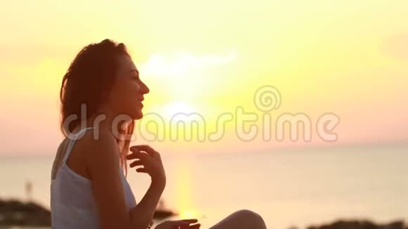 快乐的年轻女子在清晨的海滩上微笑一边想象着和太阳玩耍的情景视频的预览图